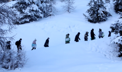 Family walking across snowy hill to cross border between Italy and France