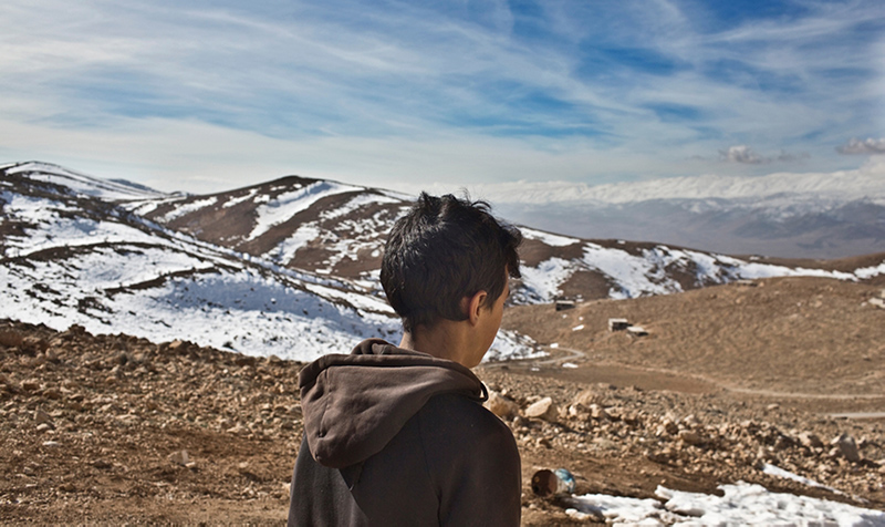 A young Syrian refugee looks out over the snow-swept mountains near the town of Arsal in Lebanon